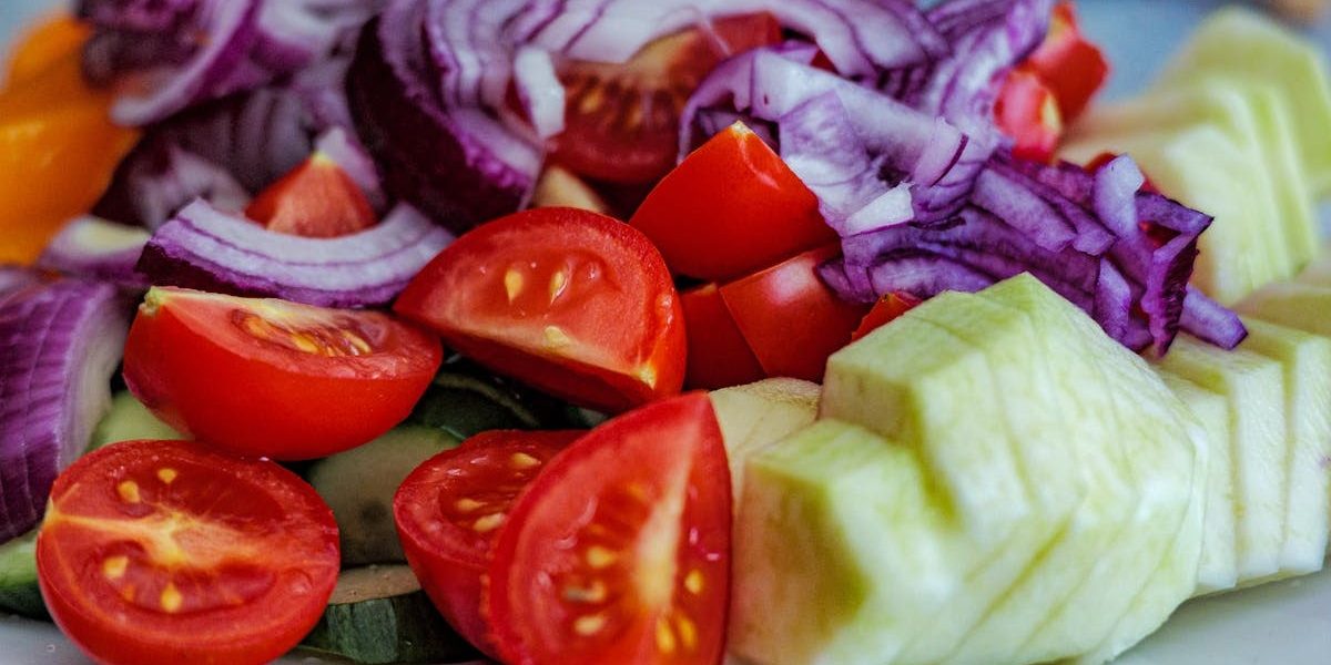 Colorful summer vegetable salad featuring tomatoes, cucumbers, and red onion slices on a plate.