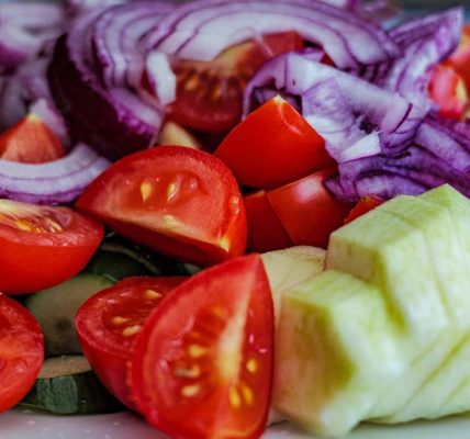 Colorful summer vegetable salad featuring tomatoes, cucumbers, and red onion slices on a plate.