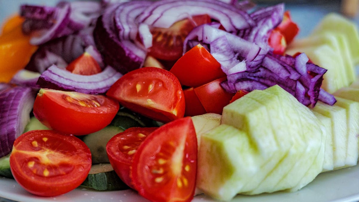 Colorful summer vegetable salad featuring tomatoes, cucumbers, and red onion slices on a plate.