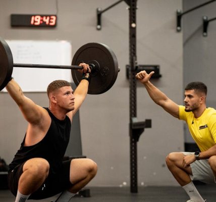 Man lifting weights under coach supervision in a gym setting, focusing on strength training.